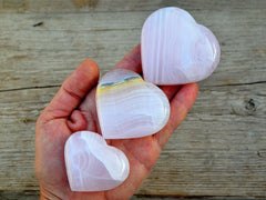 Three pink mangano calcite heartstones 50mm-65mm on hand with background with wood 