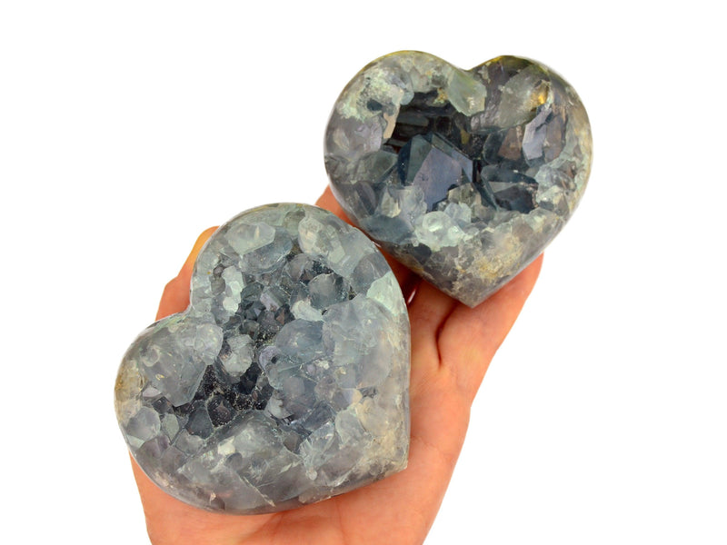 Two blue celestite druzy hearts on hand with white background