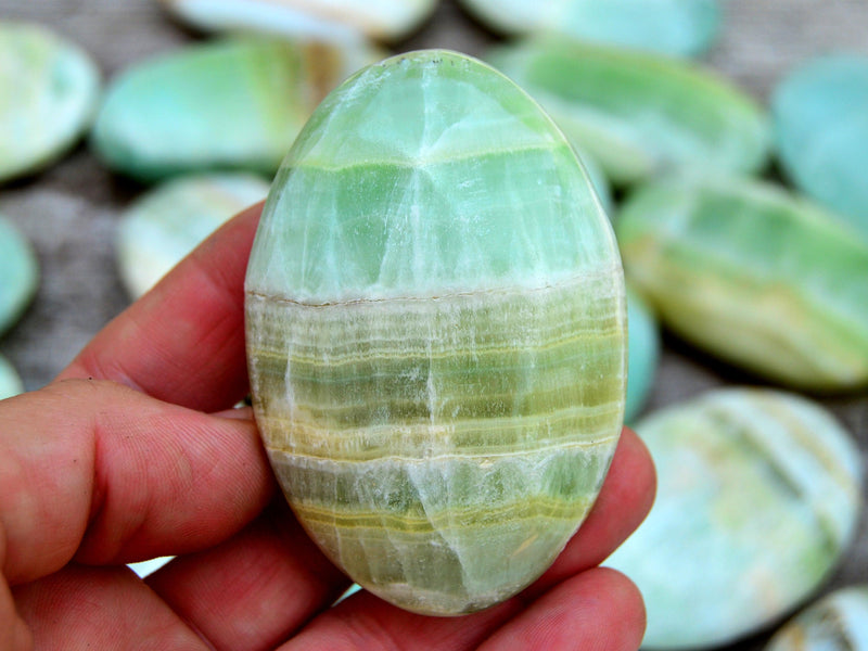 Banded green pistachio calcite 70mm on hand with background with several crystals on wood table