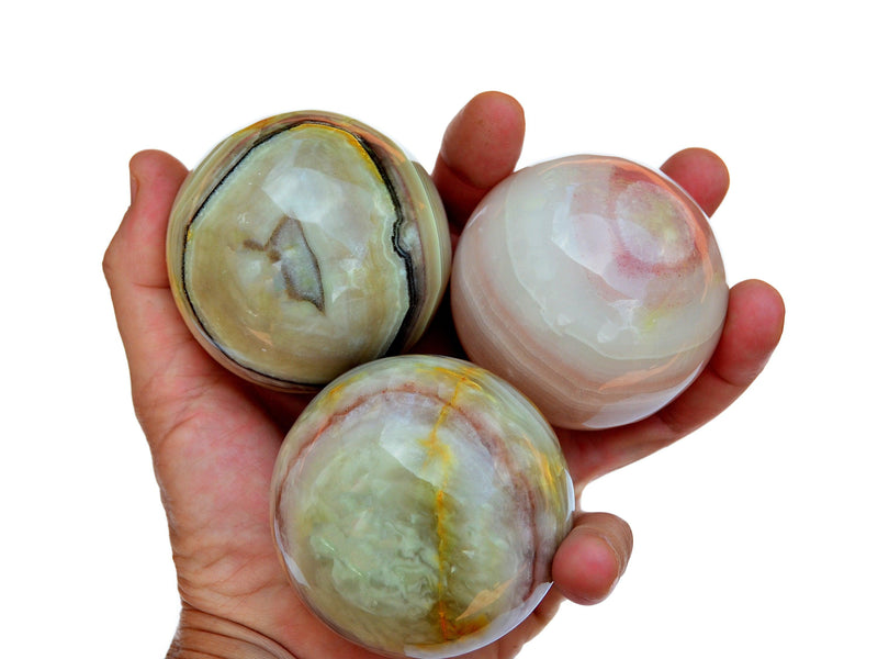 Three pink banded onyx sphere crystals 65mm on hand with white background