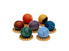 Mini spheres of polychrome jasper, carnelian, yellow septaria, chrysocolla, blue calcite, blue apatite and amethyst crystals forming a circle on wooden bases on a white background.