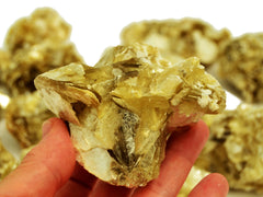 One raw muscovite crystal 70mm on hand with background with some stones on white