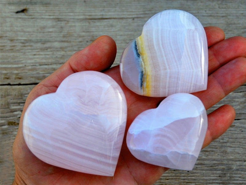 Three pink mangano calcite heart crystals 50mm-65mm on hand with background with wood 