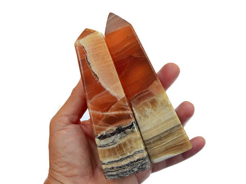 Two large banded honey calcite crystal towers 110mm on hand with white background