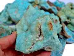 Big raw blue aragonite crystal on hand with background with some stones on white