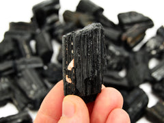 One raw black tourmaline cathedral stone 50mm on hand with background with some crystals on white