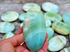 Banded green pistachio calcite 85mm on hand with background with several crystals on wood table