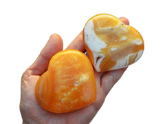 Two orange calcite crystal hearts 60mm-65mm on hand with white background