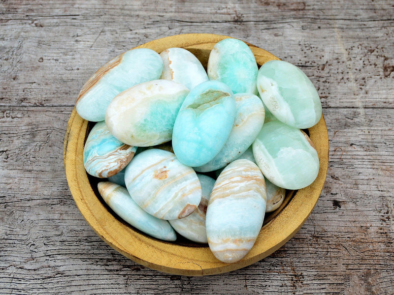 Several caribbean calcite palm stones 45mm-80mm inside a wood bowl on wood table