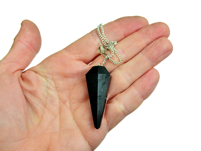 Black tourmaline faceted pendulum with silver chain on hand with white background