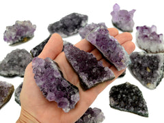 Three amethyst crystal clusters 80mm on hand with background with some druzy crystals on white