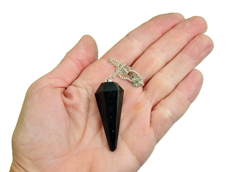 One black tourmaline faceted point pendulum on hand with silver chain and white background