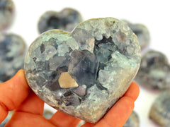 One big blue celestite druzy heart on hand with background with some stones on white