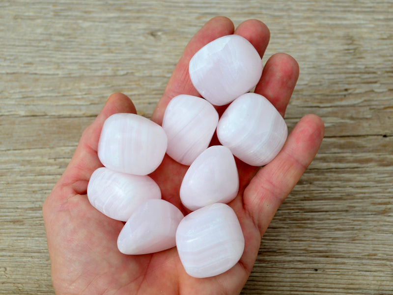 Eight pink mangano calcite cube tumbled stones on hand with wood background