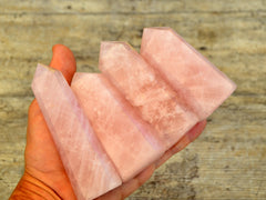 Four rose quartz polished points on hand with wood background