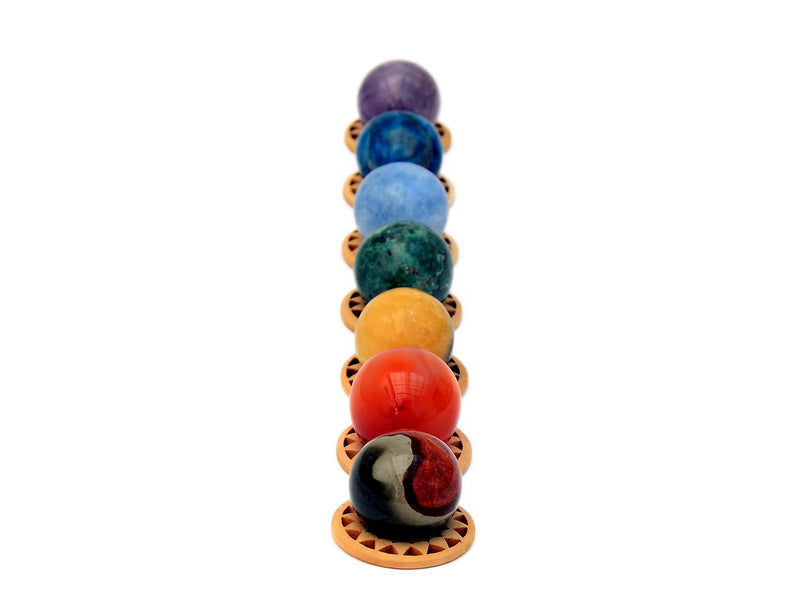 Mini spheres of polychrome jasper, carnelian, yellow septaria, chrysocolla, blue calcite, blue apatite and amethyst stones forming a vertical line on wooden bases on a white background.