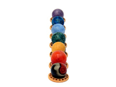 Mini spheres of polychrome jasper, carnelian, yellow septaria, chrysocolla, blue calcite, blue apatite and amethyst stones forming a vertical line on wooden bases on a white background.