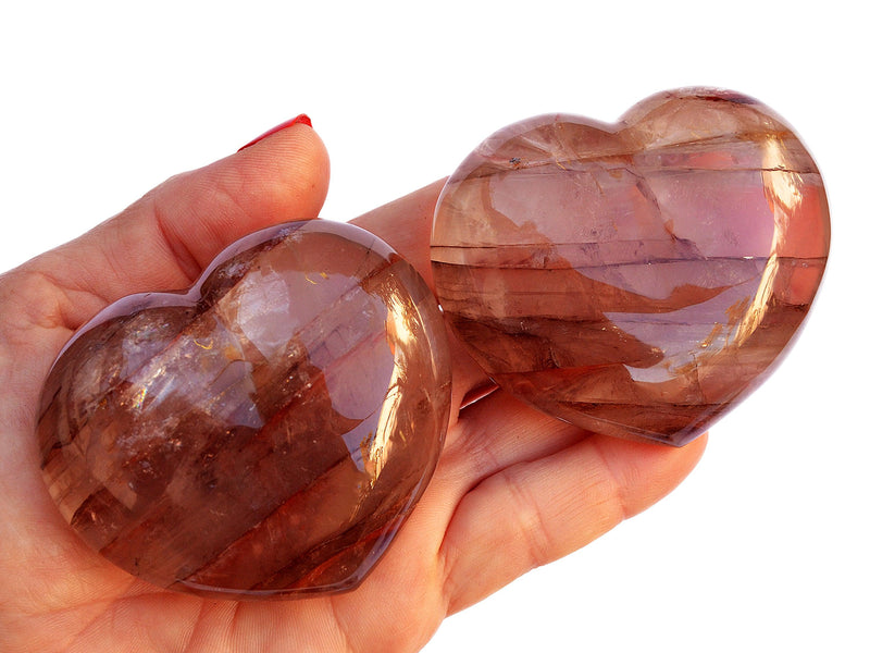 Two large hematoid quartz heart crystals 67mm on hand with white background
