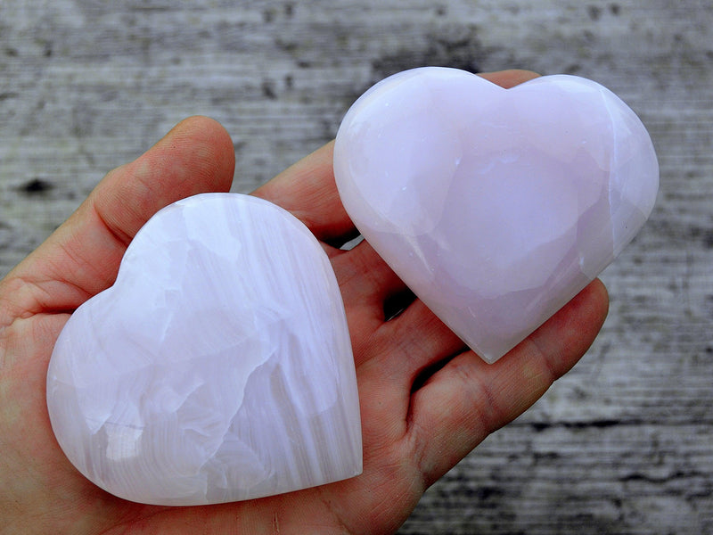 Two large pink mangano calcite hearts 65mm on hand with wood background