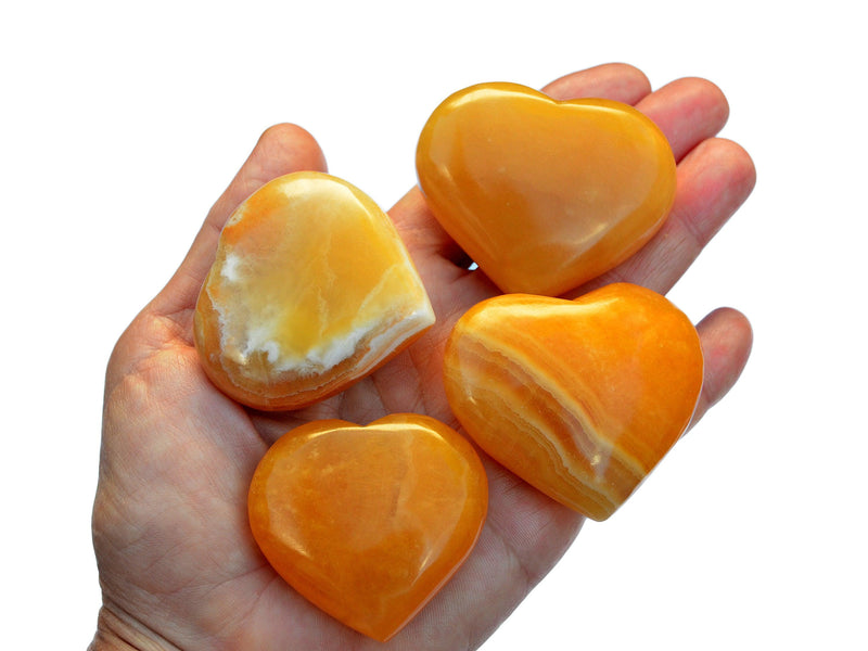 Four orange calcite crystal hearts 55mm-60mm on hand with white background