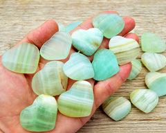 Ten green pistachio calcite crystal hearts 30mm-35mm on hand with background with some hearts on wood table