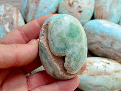 One druzy green blue aragonite palm stones 80mm on hand with background with some crystals