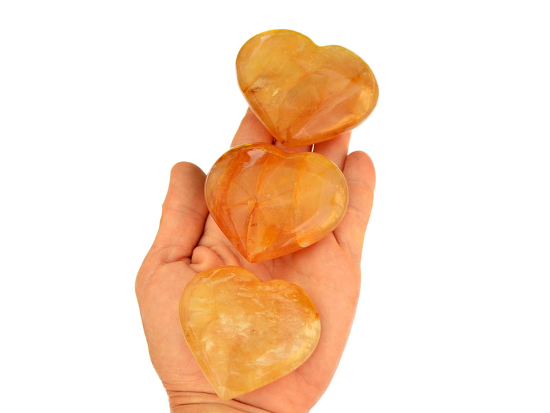 Three large yellow hematoid quartz hearts on hand with white background