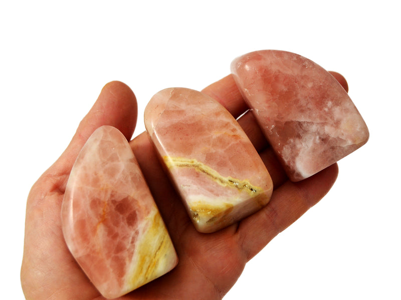 Three rose calcite free forms 40mm on hand with white background