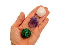 One small tumbled mangano calcite stone, raw amethyst and chrycolla sphere on hand with white background 