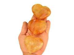 Three large yellow hematoid quartz hearts on hand with white background