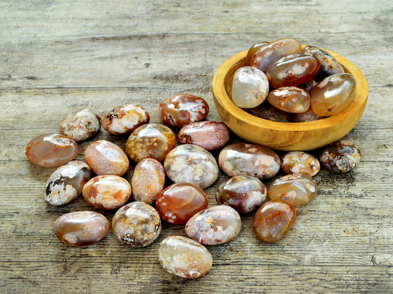 Several flower agate palm stones on wood table and some crystals inside a wood bowl