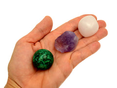 One small tumbled mangano calcite crystal, raw amethyst and chrycolla sphere on hand with white background 