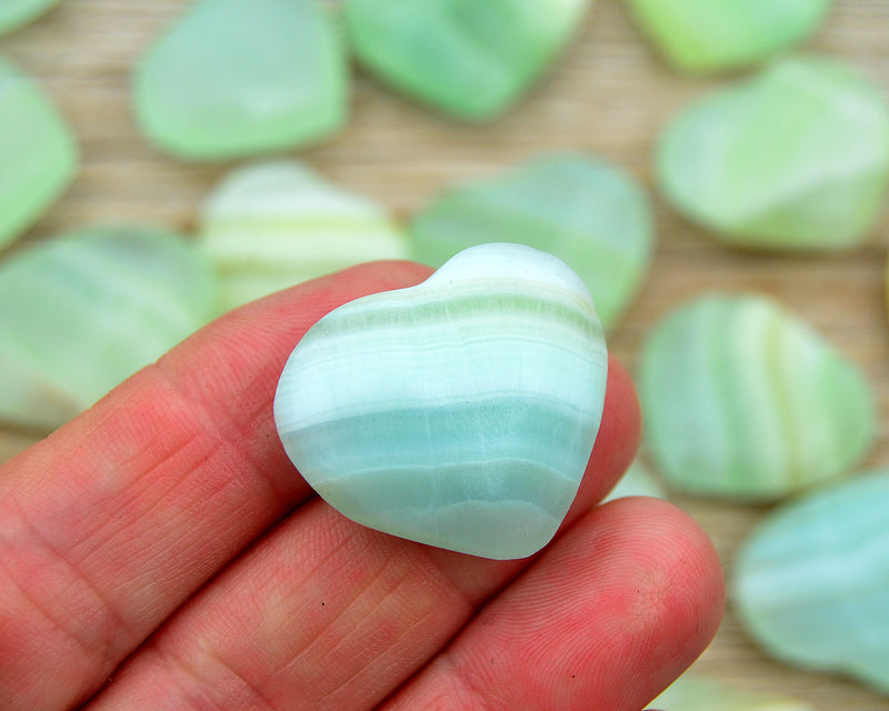 One green pistachio calcite crystal hearts 30mm on hand with background with some heart on wood table