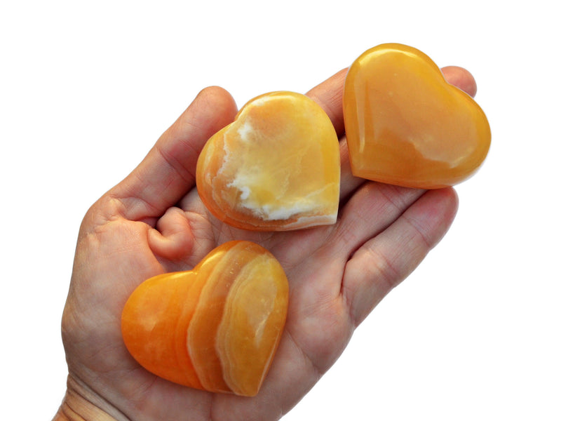 Three orange calcite crystal hearts 45mm-55mm on hand with white background