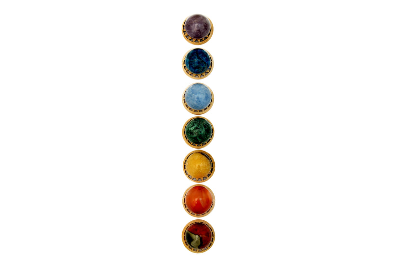Mini spheres of polychrome jasper, carnelian, yellow septaria, chrysocolla, blue calcite, blue apatite and amethyst stones forming a vertical line on wooden bases on a white background.