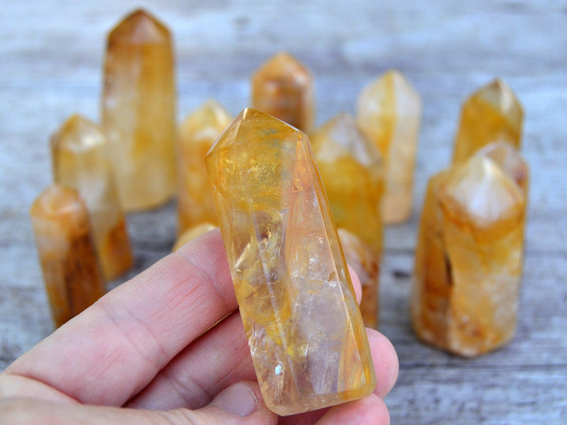 One samall golden healer quartz prism on hand with background with several towers on wood