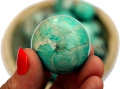 One amazonite sphere stone 25mm on hand with background with some crystals inside a wood bowl