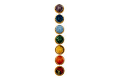 Mini spheres of polychrome jasper, carnelian, yellow septaria, chrysocolla, blue calcite, blue apatite and amethyst stones forming a vertical line on wooden bases on a white background.