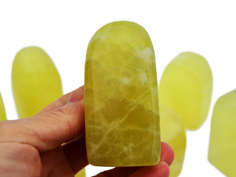 One lemon calcite free form stone 90mm on hand with background with some crystals on white