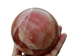 Extra large rose calcite crystal ball 95mm on hand with white background