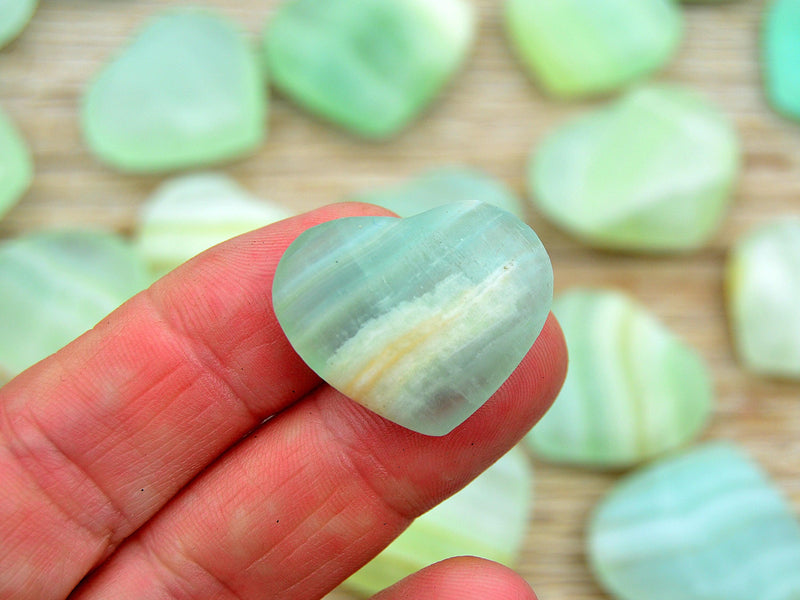 One mini green pistachio calcite mineral heart shapped 30mm on hand with background with some hearts on wood table