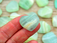 One mini green pistachio calcite mineral heart shapped 30mm on hand with background with some hearts on wood table