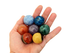 Mini spheres of polychrome jasper, carnelian, yellow septaria, chrysocolla, blue calcite, blue apatite and amethyst stones on hand with white background
