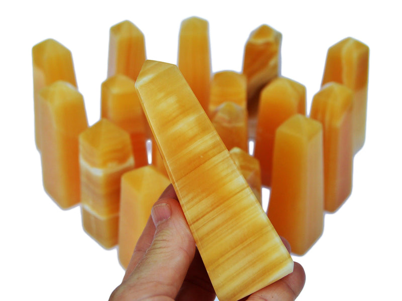 One banded orange calcite tower 115mm on hand with background with several obelisks