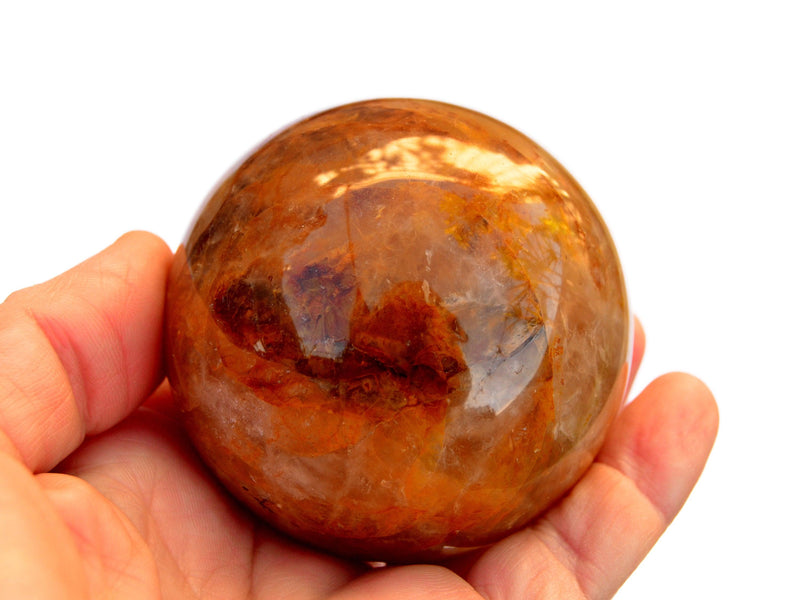 One golden healer qyartz crystal sphere 75mm on hand with white background