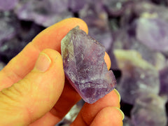 One raw purple amethyst stone 30mm on hand with background with some crystals