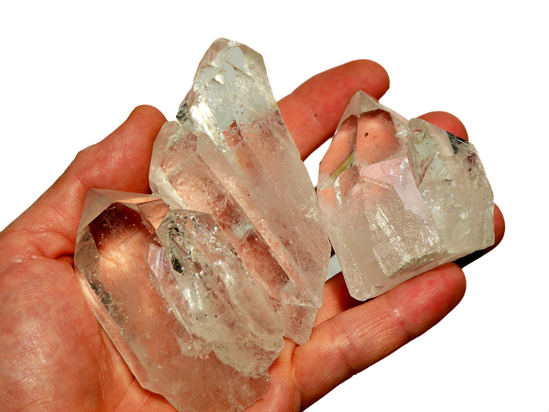 Hand holding three clear quartz point rocks against a white background