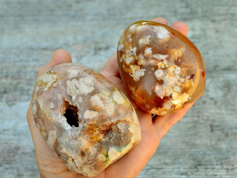 Two large flower agate free form crystals on hand with wood background