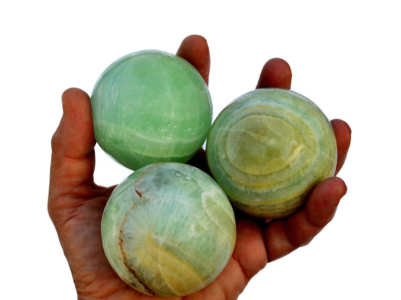Three pistachio calcite spheres 40mm - 60mm on hand with white background