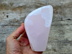 One big pink mangano calcite free form stone 140mm on hand with wood background